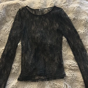 Svart spetsblus med lång ärm från Nelly - Säljer en svart, transparent spetsblus med lång ärm från Nelly. Blusen har rund halsringning och är gjord i ett tunt, detaljerat spetsmaterial som ger en cool och edgy vibe. Perfekt att styla lager på lager eller med ett linne under för extra effekt.
