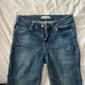 Blå jeans med trekvartsmodell - Snygga blå jeans från Lindex med klassisk femficksdesign och trekvarts raka ben. Jeansen har normal midja, tydliga kontrastsömmar och en stilren look som passar till det mesta. Materialet är slitstarkt jeans och färgen är en cool mellanblå ton.