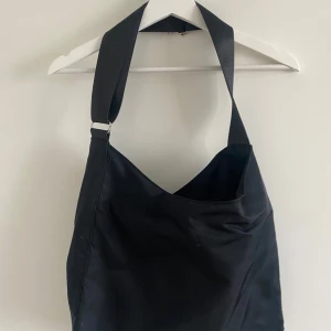 Svart axelväska i polyester - Stilren svart axelväska med bred axelrem och enkel design. Väskan är tillverkad i polyester och har en mjuk, slouchy form som gör den perfekt för att bära med sig allt man behöver. Passar dig som gillar minimalistisk stil. Axelrem går att skjustera. 