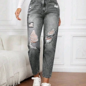 Gråa ripped high waist jeans - Snygga grå jeans med hög midja och slitna detaljer på benen. Modellen är rak och har en cool, avslappnad vibe med stora hål och fransiga kanter. Perfekt för dig som gillar streetstyle och vill sticka ut lite extra.