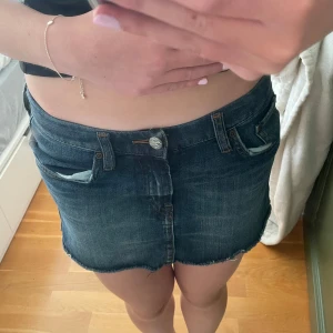 Mörk jeanskjol från H&M L.O.G.G. - Snygg mörkblå jeanskjol från H&M L.O.G.G. med rå kant nertill och klassiska fem fickor. Kjolen har bälteshällor, knapp och dragkedja framtill. Perfekt för dig som gillar en chill och trendig stil. Kjolen är i storlek 152 men passar mig som vanligtvis har XS ibland S. 