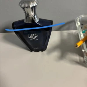 Turathi parfym från Afnan - Snygg parfymflaska från Afnan, modell Turathi. Flaskan är mörkblå med silverfärgad, elegant kork och har en modern, kantig design. Perfekt för dig som gillar exklusiva dofter och stilren look på parfymhyllan.