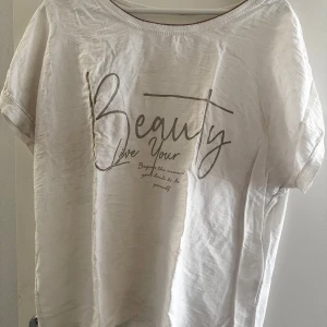 Vit t-shirt med texttryck - Vit t-shirt med rund hals och korta ärmar. Framsidan har ett snyggt texttryck med orden 'Beauty Live Your'. T-shirten är gjord i mjuk bomull och har en avslappnad passform.