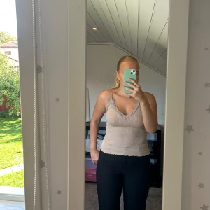 Beige ribbad linnetopp med spets - Säljer en beige ribbad linnetopp med smala axelband och v-ringad hals. Toppen har en snygg spetskant i ljusgrått längs halsringningen och en lite fläck som (andra bilden). Djur finns i hemmet! 🩷 