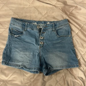 Blå jeansshorts från LAB Industries - Snygga blå jeansshorts från LAB Industries med klassisk femficksdesign och knappgylf framtill. Modellen är högmidjad och har en normal passform. Perfekta för varma dagar och enkla att matcha med din favorit-t-shirt eller hoodie.