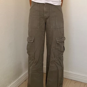 Gröna cargojeans  - Säljer ett par snygga gröna/grå cargopants från Weekday med bred passform och medelhög midja 💚🏙️✨De har raka ben och stora fickor både fram, på benen och bak. Tillverkade i 100 % bomull. 