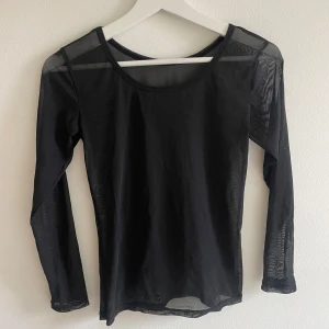 Svart mesh långärmad topp - Obs saknas storlekslapp men skulle uppskatta den till storlek S. Säljer en svart långärmad mesh topp med rund hals. Tunn och transparent, perfekt för lager-på-lager eller att styla med coola accessoarer. Materialet är syntet och ger en edgy vibe. Passformen är normal och toppen är helt utan mönster eller detaljer.