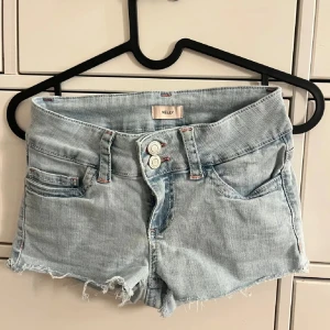 Ljusblå jeansshorts  - Snygga ljusblå jeansshorts från Nelly med fransig kant och dubbla knappar framtill. Rosa detaljer på bakfickan. Storlek 32. Aldrig använd svara tvättade en gång.