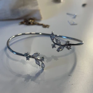 Silverfärgat armband med kristaller - Ett elegant armband i silverfärg med gnistrande kristaller formade som blad och små blommor. Armbandet har en tunn, stilren design och detaljer som ger en lyxig känsla. Perfekt för dig som gillar smycken med naturinspirerade detaljer.