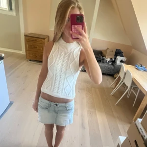 Vit stickad croppad polotopp - Säljer en vit stickad croppad polotopp med snyggt kabelmönster och ribbad hög hals. Toppen är ärmlös och har en cool, lite chunky känsla som passar perfekt till jeans eller kjol. Perfekt för dig som gillar trendiga och bekväma plagg! Så fin men kommer aldrig till användning❤️