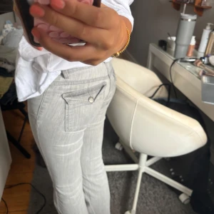 Ljusgrå bootcut jeans med fickdetaljer - Snygga ljusgrå jeans från Nelly med bootcut passform och coola fickdetaljer med knappar bak. Jeansen har väldigt låg midja och är gjorda i mjukt jeansmaterial med stretch. Storlek 34!