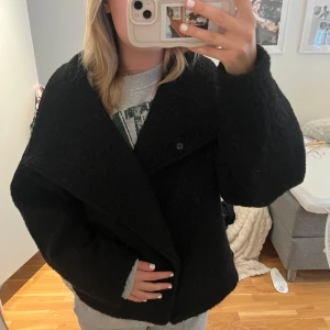 Svart teddyjacka med bred krage - Säljer en svart teddyjacka med bred krage och dubbla knappar framtill. Jackan har en loose passform och är tillverkad i mjukt teddy-material som ger en cool och mysig vibe. Perfekt för dig som gillar oversized look och vill ha något som sticker ut.