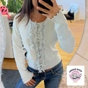 Ljusblå kofta med volang och knappar - Supersöt ljusblå kofta med volangdetaljer längs knäppningen framtill och dekorativa knappar på ärmsluten. Tröjan har rund hals, ribbade muddar och är långärmad. Perfekt för dig som gillar romantisk och feminin stil.