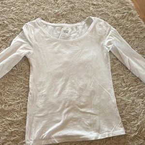 Vit långärmad tröja från öager 157 - En enkel och stilren vit långärmad tröja från lager 157 med rund halsringning. Perfekt att ha som basplagg och lätt att matcha med andra kläder. Tillverkad i mjuk bomull som känns skön mot huden. Storlek xs, inga fläckar: använd 1 gång.