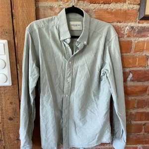 Ljusgrå beige skjorta från These Glory Days - Snygg ljusgrå skjorta från These Glory Days i storlek L. Klassisk modell med knappar hela vägen, button down-krage och långa ärmar. Skjortan är tillverkad i mjuk bomull och har en stilren, enkel look som funkar till många olika outfits.