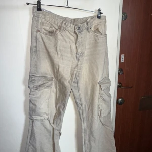 Beige cargopants från Zara, strl 40 - Säljer ett par beige cargopants från Zara i storlek 40. Byxorna har flera stora fickor på benen och bak, samt breda ben med en loose passform. Materialet är bomull och färgen är ljusbeige, perfekt för en chill och avslappnad stil.