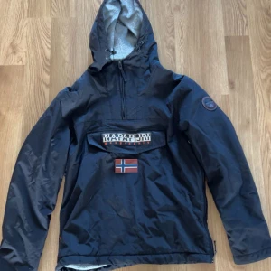Svart vinterjacka  - Svart vinter från Napapijri med stor huva och halv dragkedja. Jackan har fleecefoder i luvan vilken håller den väldigt varm. Jacka är i toppen skick utan defekter!!! Hör av dig vid frågor