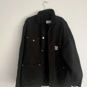 Svart Carhartt overshirt L - Svart overshirt från Carhartt Work In Progress i storlek L. Jackan har flera fickor med tryckknappar framtill och klassisk krage. Materialet är slitstark bomull och passformen är loose, perfekt för lager på lager. Snygg logga på bröstfickan. Sitter baggy. Nypris var runt 1900kr.