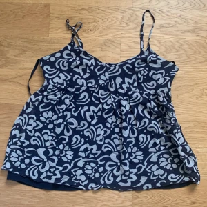 Blommig  linnetopp från INC - Supersöt marinblå linnetopp med ljusblå blommigt mönster från INC. Tunn och lyxig känsla i 100% silke med polyesterfoder. Justerbara smala axelband och dragkedja i sidan för enkel påklädning. Perfekt för dig som gillar chill och stilren vibe.