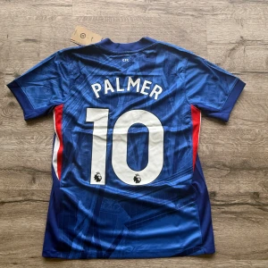 Chelsea Palmer #10 Nike fotbollströja - Chelsea FC matchtröja med Palmer och nummer 10 på ryggen. Tröjan är blå med vita och röda detaljer, har korta ärmar och är tillverkad i lätt, ventilerande polyester. Snyggt geometriskt mönster på framsidan, Chelsea-emblem och Nike-logga. Perfekt för dig som älskar Premier League. Storlek: S helt ny med prislapp. Priset är inte hugget i sten så skicka pm vid funderingar.