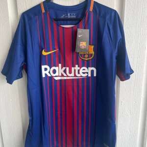 FC Barcelona Messi tröja Nike M - Säljer en officiell FC Barcelona matchtröja från Nike med Messi 10 på ryggen. Tröjan är blå med röda vertikala ränder, gula detaljer och klubbmärke på bröstet. Kortärmad och tillverkad i lätt, ventilerande polyester. La Liga-märke på ärmen och Rakuten-tryck på framsidan.