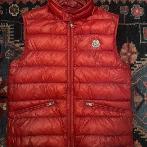 Moncler Väst röd - Hej,  Till salu: en Moncler väst i storlek 3 (M), klassisk röd färg. Västen är i mycket bra skick och erbjuder både stil och komfort. Säljes till ett riktigt bra pris!  Hör av dig om du har några frågor eller vill se fler bilder.