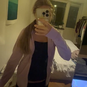 Ljuslila velour hoodie med bling - Säljer en ljuslila hoodie från Juicy Couture i mjuk velour med glittrig broderad logga och strassdetaljer på ryggen. Jackan har huva, dragkedja framtill och långa ärmar. Perfekt för dig som gillar bling och comfy vibes.