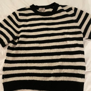 Randig stickad tröja från H&M - Säljer en svartvit randig stickad tröja från H&M i storlek M. Tröjan har korta ärmar, rund hals och är gjord i ett mjukt stickat material. Perfekt för dig som gillar klassiska mönster och vill ha en chill look.