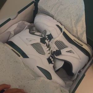 Nike Jordan 4 sneakers vit/grön - Säljer ett par Nike Jordan 4 sneakers i fräsch vit och mörkgrön färg. Skorna har snygga meshpaneler, klassisk snörning och detaljer i grönt på sula och öglor. Ovandelen är i skinn och de har en platt sula med synlig Air-enhet. Perfekt för dig som vill ha en ikonisk och stilren look.