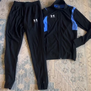 Helt ny svart o blå under armour dress  storlek S/M - Svarta träningsbyxor från Under Armour med vit logga på låret. Byxorna har en slim passform och är gjorda i ett lätt och stretchigt syntetmaterial som är perfekt för träning. Elastisk midja och dragkedja vid benslut för extra komfort.
