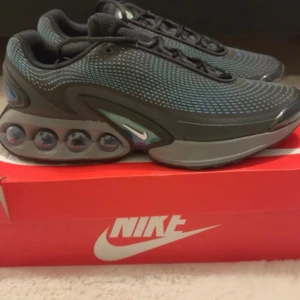 Nike Air Max Dn sneakers  - Nike Air Max sneakers med futuristisk design och synliga luftkuddar i sulan. Svart mesh-överdel med blå och gröna detaljer, små vita och blå swoosh-loggor, och snörning. Snyggt mönstrad ovandel och robust platt sula för extra komfort. Perfekt för dig som gillar streetstyle. Passar bra till träning som till vardag 