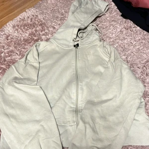 Ljusgrön hoodie med dragkedja - Säljer en enkel och stilren ljusgrön hoodie med dragkedja framtill och huva. Jackan har långa ärmar och ribbade muddar vid ärmslut och nederkant. 