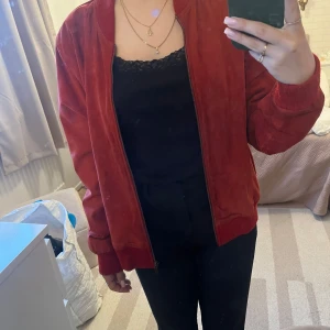 Röd skinnjacka från Voice of Europe - Säljer en snygg röd läderjacka från Voice of Europe i äkta läder. Jackan har dragkedja framtill, ribbade muddar och krage samt två fickor på sidorna. Perfekt för dig som vill ha en stilren och trendig look.