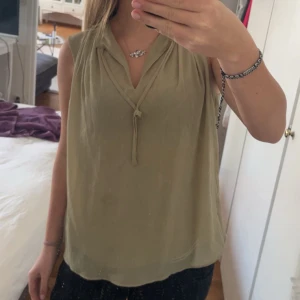 Beige grön ärmlös blus från H&M - Säljer en stilren grön beige ärmlös blus från H&M med v-ringning och knyt framtill. Perfekt för varma dagar och enkel att matcha med olika nederdelar. Luftigt material som känns skönt mot huden. Tveka inte på att höra av er om det är något ni undrar💕