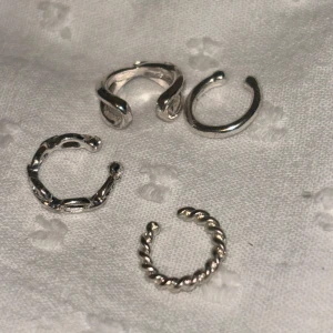 Fyra silvriga ear cuffs i olika mönster - Säljer ett set med fyra silvriga ear cuffs i olika designer. En är tvinnad, en har ett vågigt mönster, en är slät och en har ett flätat utseende. Perfekta för att mixa och matcha för en unik stil.