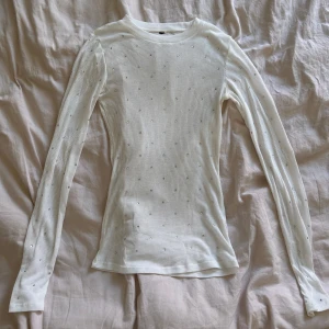 Vit genomskinlig långärmad topp med pärlor - Säljer en vit ribbad långärmad topp med små pärlor över hela tröjan. Tight passform och rund halsringning. Perfekt för dig som gillar enkla men ändå detaljerade plagg. Bortklippt lapp men sitter som S. bara använd en gång 