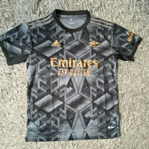 Arsenal svart bortatröja - Säljer en svart Arsenal bortatröja från Adidas med guldiga detaljer. Nyskick, aldrig använt. Inga tryck på ryggen. Strl L, passar även M