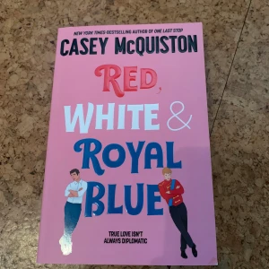Red, White & Royal Blue - En populär romantisk roman på engelska med rosa omslag och illustrationer av två unga män. Boken är skriven av Casey McQuiston och har titeln 'Red, White & Royal Blue' i stora färgglada bokstäver. Perfekt för dig som gillar feelgood och kärlekshistorier.
