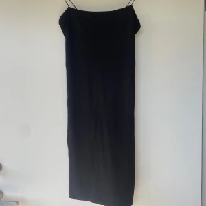 Svart långklänning med smala axelband från NA-KD - Säljer en svart knälång från NA-KD med smala axelband och enkel, stilren design. Perfekt för dig som gillar minimalistisk stil. Klänningen har en rak passform och är tillverkad i ett mjukt, slätt material.