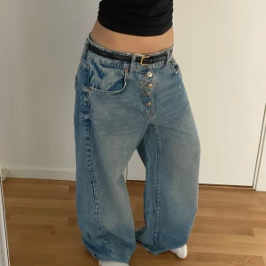 Blå wide leg jeans från Zara - Säljer ett par ljusblå jeans från Zara med breda ben och mid/låg midja. Byxorna har knappar framtill och klassiska fickor både fram och bak. Perfekta för dig som gillar en avslappnad och trendig stil. (Byxorna kommer utan bältet)