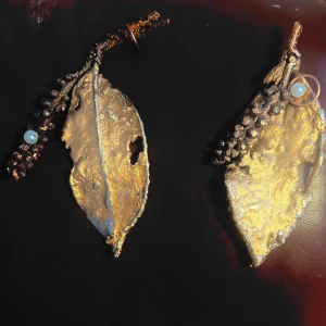 Guldiga lövformade örhängen med pärldetaljer - Unika örhängen i form av löv med guldig yta och små pärldetaljer längs kanten. Designen är inspirerad av naturen och har en konstnärlig känsla. Perfekta för dig som vill sticka ut med ett smycke som drar blickarna till sig.