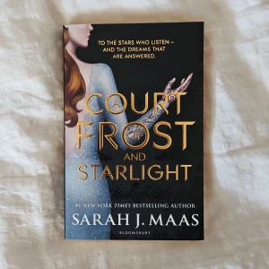 A Court of Frost and Starlight - Fantastisk fantasybok på engelska av Sarah J. Maas. Omslaget har en mörk bakgrund med guldtext och en illustrerad kvinna i blå klänning med dekorativa detaljer. Perfekt för dig som gillar magi, äventyr och romantik.