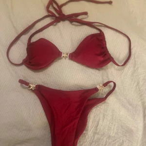 Vinröd bikini med gulddetaljer - Snygg vinröd bikini med knyt i nacken och dekorativa guldfärgade detaljer både på överdelen och underdelen. Perfekt för sommaren! Aldrig provad eller använd. Helt ny.