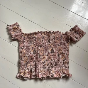 Blommig offshoulder topp i rosa toner - Säljer en söt offshoulder topp med blommigt mönster i rosa, beige och bruna nyanser. Toppen har smockad passform och volangkant nertill och upptill. Perfekt för varma dagar och ger en romantisk vibe. Blir bättre pris vid köp av flera. Skriv för fler bilder🩷