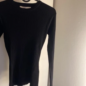 Svart ribbad långärmad tröja från NA-KD - Säljer en svart, tight och ribbad långärmad tröja från NA-KD. Perfekt basplagg med rund halsringning och smal passform. Enkel att styla till olika outfits och superbekväm att bära.