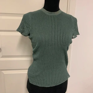 Grön ribbad kortärmad topp - Säljer en grön ribbad topp med korta ärmar och rund halsringning. Tröjan har ett genomgående ribbat mönster och är tillverkad i ett stretchigt material som sitter figurnära. Perfekt för lager-på-lager eller som den är. Den är från Zara storlek S men lappen är bortklippt 