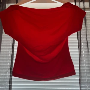 Röd tröja med öppen rygg - Säljer en snygg röd offshoulder topp med bred urringning. Toppen har en figurnära passform och är perfekt för dig som vill sticka ut med en enkel men trendig look.