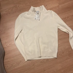 Vit stickad tröja med dragkedja - Säljer en stilren vit stickad tröja från H&M med hög krage och dragkedja framtill. Perfekt för lager-på-lager och passar till många olika outfits. Tröjan har lång ärm och ribbade muddar. Nypris 349kr