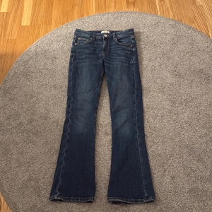 Blå bootcut jeans från Gina Tricot - Säljer ett par klassiska blå jeans från Gina Tricot i modell bootcut. Jeansen har fem fickor, dragkedja och knapp framtill samt snygga sömmar. Perfekta för dig som gillar en tidlös jeansstil med lite utsvängda ben.