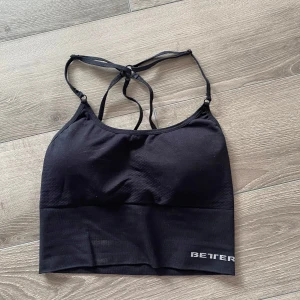 Svart topp från Better Bodies - Svart sportig linnetopp från BB med smala axelband som korsas i ryggen. Perfekt för träning eller en aktiv vardag. Enkel design med logga framtill. Snygg och bekväm passform.